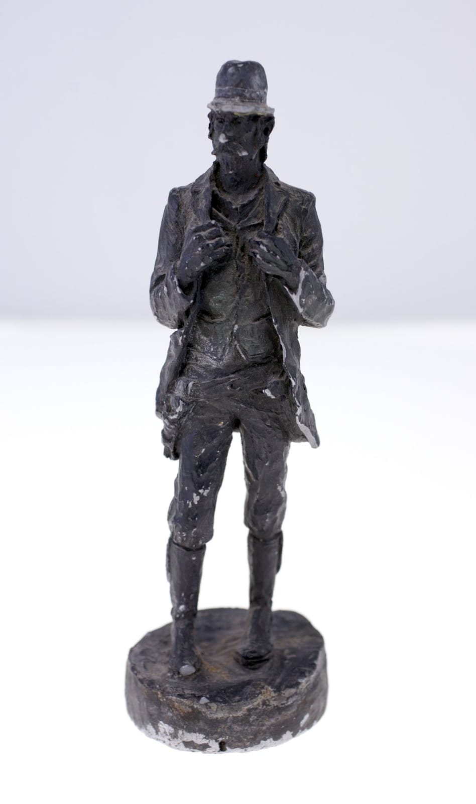 Small cast figurative sculpture of a standing man in hat and coat